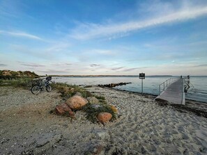 Ein Küstenweg mit einem Fahrrad links, einem Wegweiser rechts und Blick auf das Meer und entfernte Gebäude.