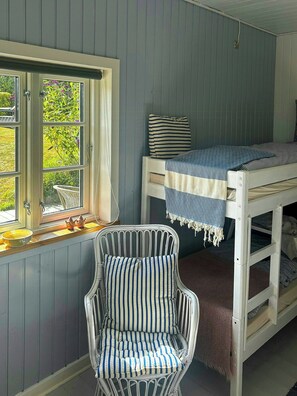 Ein Zimmer mit einem Etagenbett, einem Sessel und einem fenster mit Vorhängen.