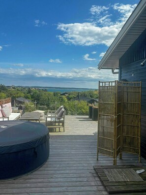 Eine Holzterrasse mit Whirlpool, Sitzbereich und Blick auf die Landschaft.