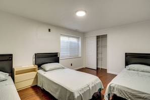 A bedroom with two single beds, a bedside table, a window with blinds, and a door leading to a closet. - Gateway to Mountain Fun! 5BR Utah Home (Lehi)