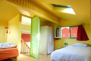 Ein Zimmer mit zwei Betten, einem Fenster mit rotem Vorhang, einer Tür zu einem anderen Raum und einer Deckenleuchte.