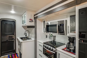 A compact kitchen with a built-in microwave, oven, and sink. - Hot Tub, Picnic Area: RV Stay in Carlsbad (Carlsbad)