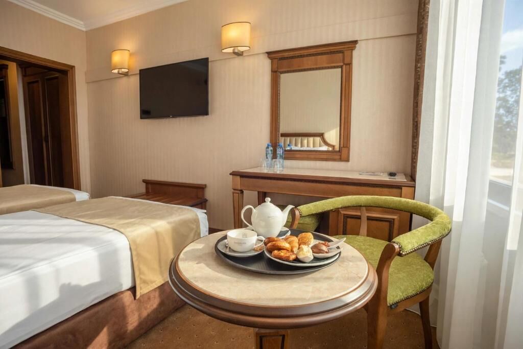 A hotel room with two beds, a dining table with breakfast, a TV, and a mirror.