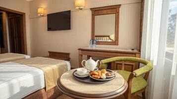 A hotel room with two beds, a dining table with breakfast, a TV, and a mirror.