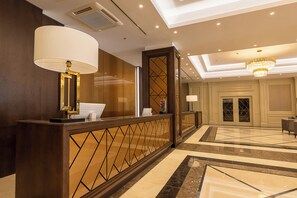 Een hotellobby met een receptiebalie, een kroonluchter en een incheckbalie.