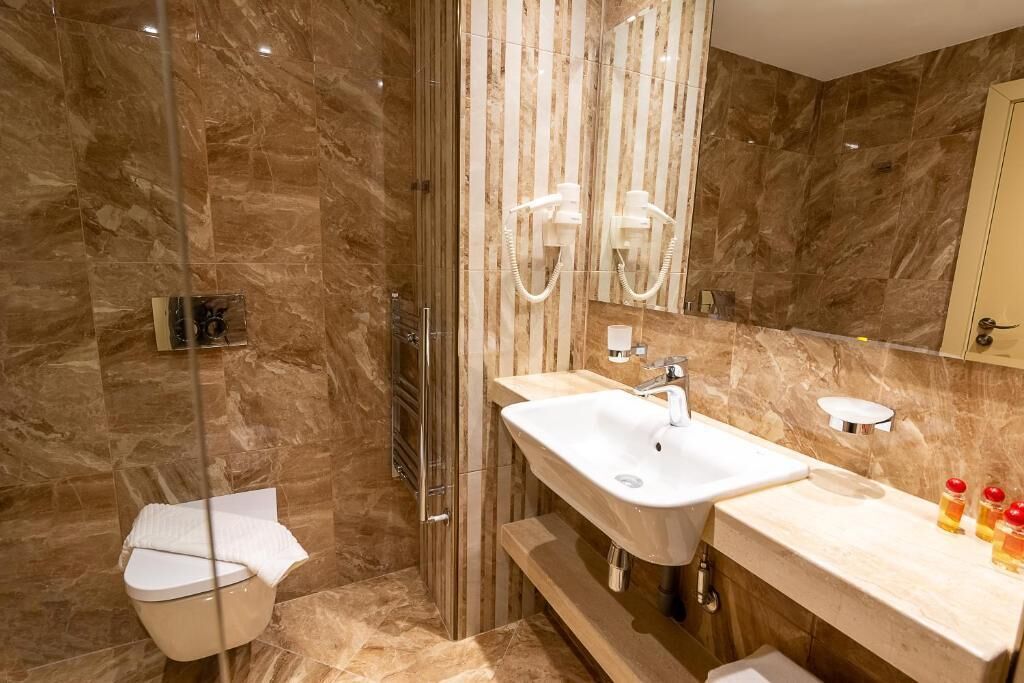 A modern bathroom with a glass-enclosed shower, a white sink with a mirror, and a toilet.