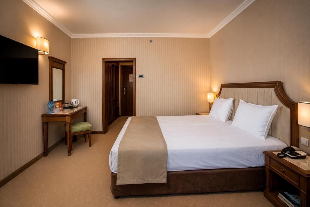 A hotel room with a bed, bedside table, lamp, and a television mounted on the wall.