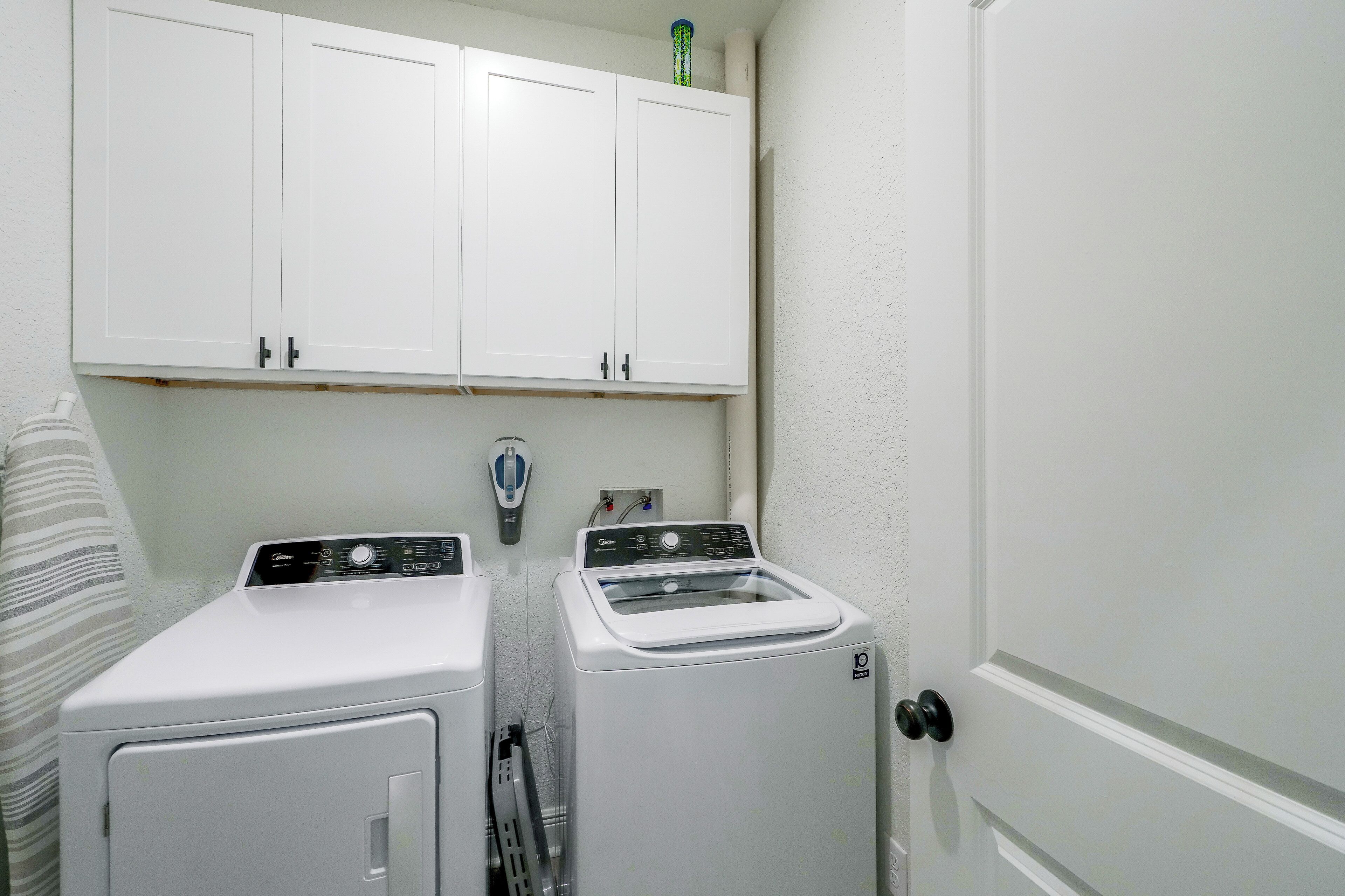 Une buanderie équipée de deux machines à laver, d’un sèche-linge et d’un meuble de rangement au-dessus.