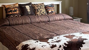 A bedroom with a large bed, multiple pillows, a mounted artwork of bulls, and a chandelier.