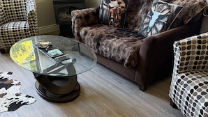 A cozy living room with a fur-covered sofa, patterned chairs, a glass coffee table, and a fireplace.