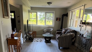 A spacious living room with a wooden floor, a round coffee table, a patterned sofa, and a dining area with wooden chairs and a table.