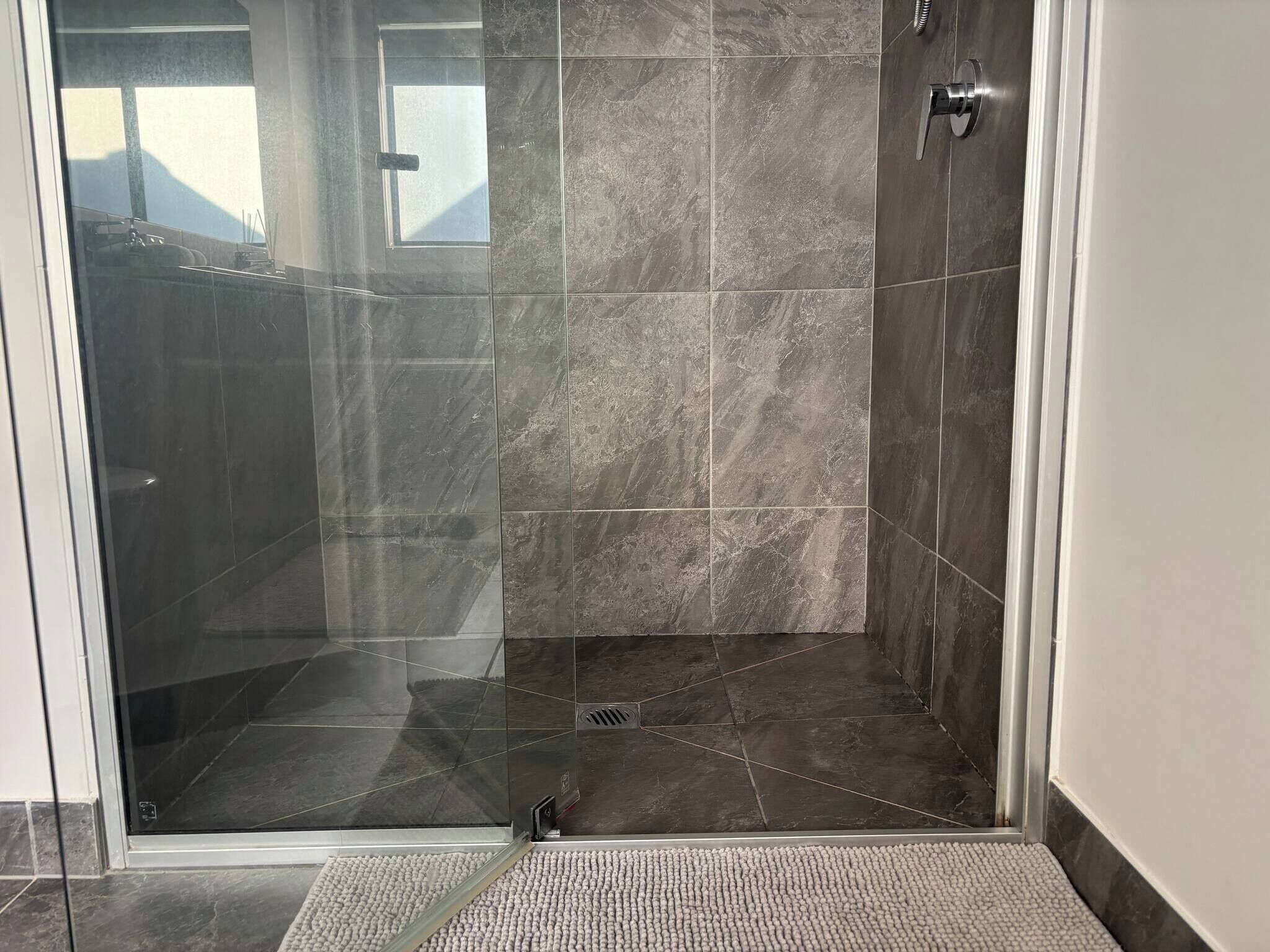 A glass-enclosed shower area with dark tiles and a visible drain.