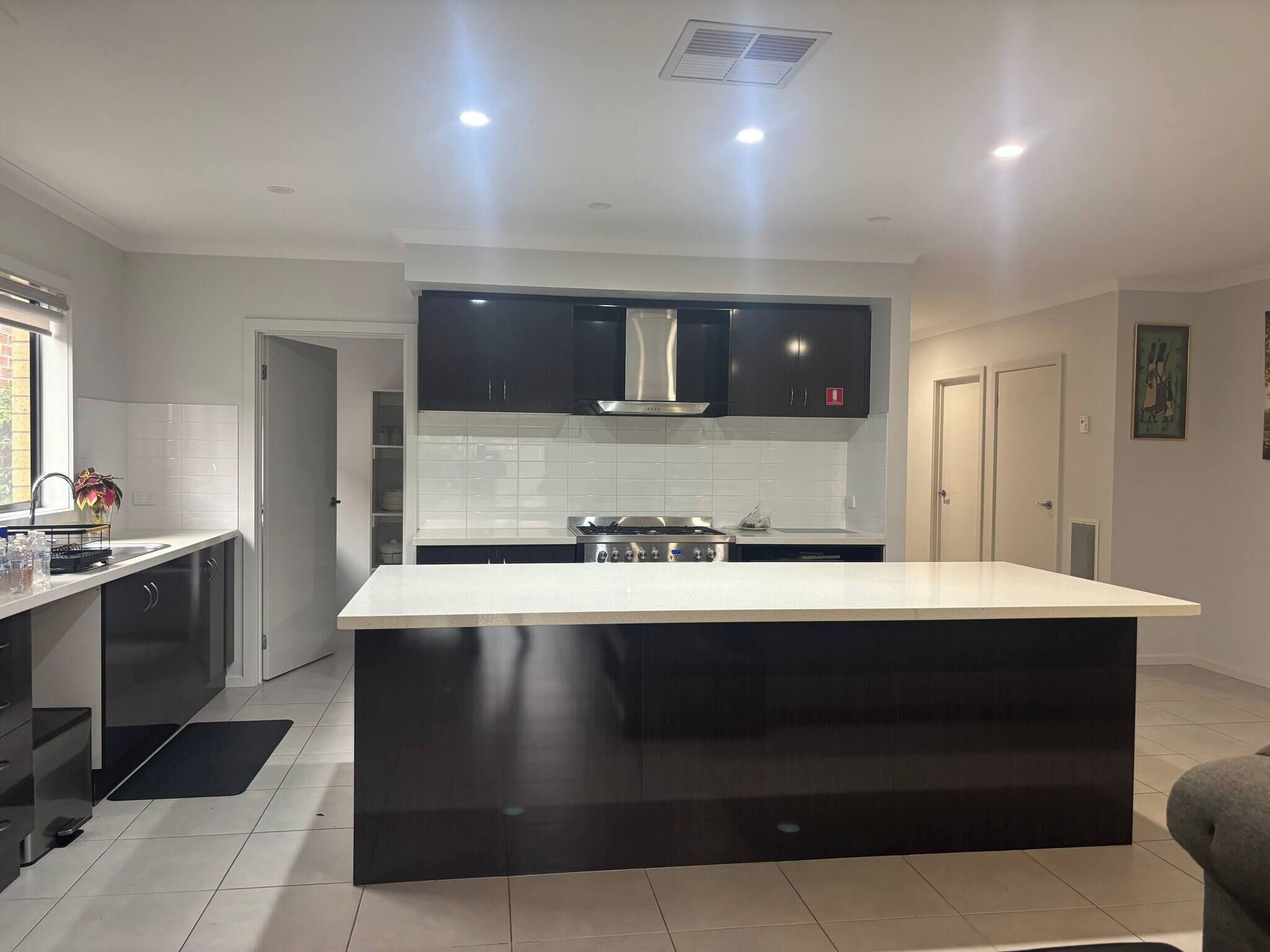 A modern kitchen with a central island, dark cabinetry, and a stainless steel range hood.
