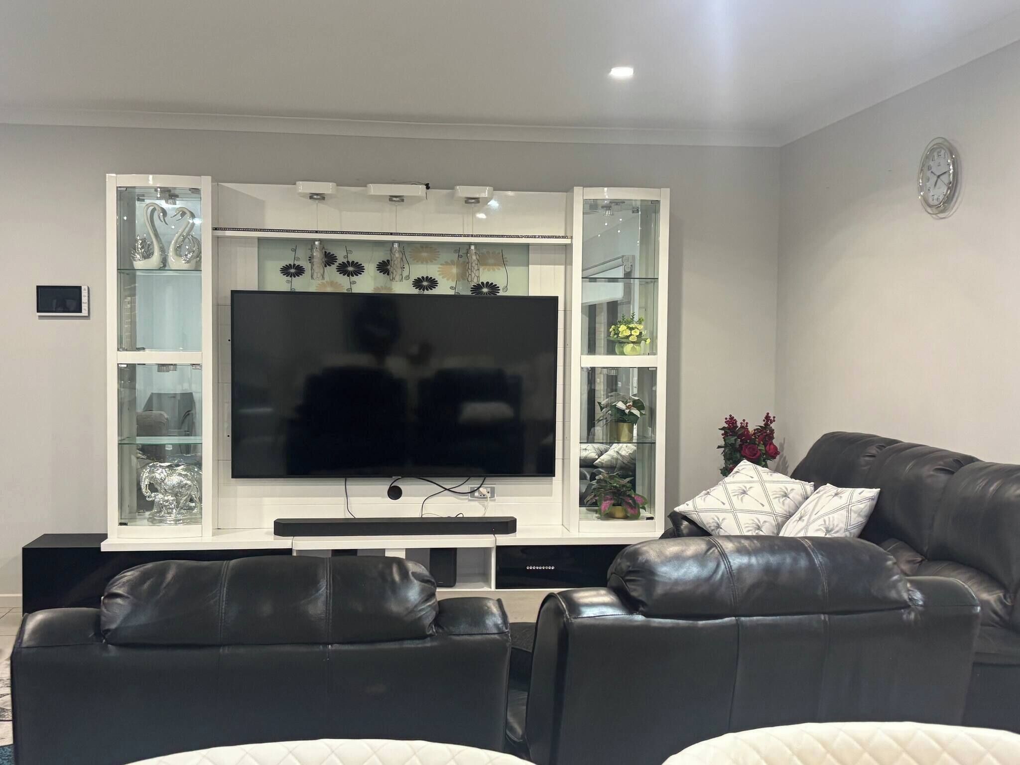 Un salon doté d’un grand téléviseur à écran plat fixé à un meuble blanc aux portes vitrées, de canapés en cuir et d’objets décoratifs.