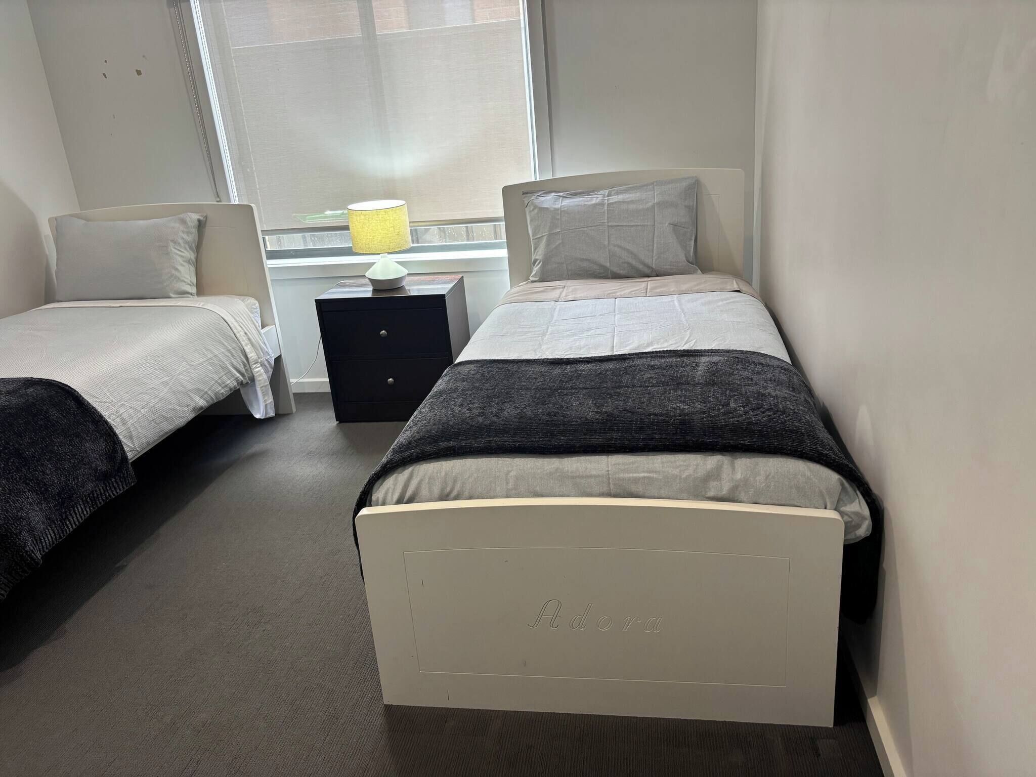 Een hotelkamer met twee eenpersoonsbedden, een nachtkastje met een lamp en een raam met jaloezieën.