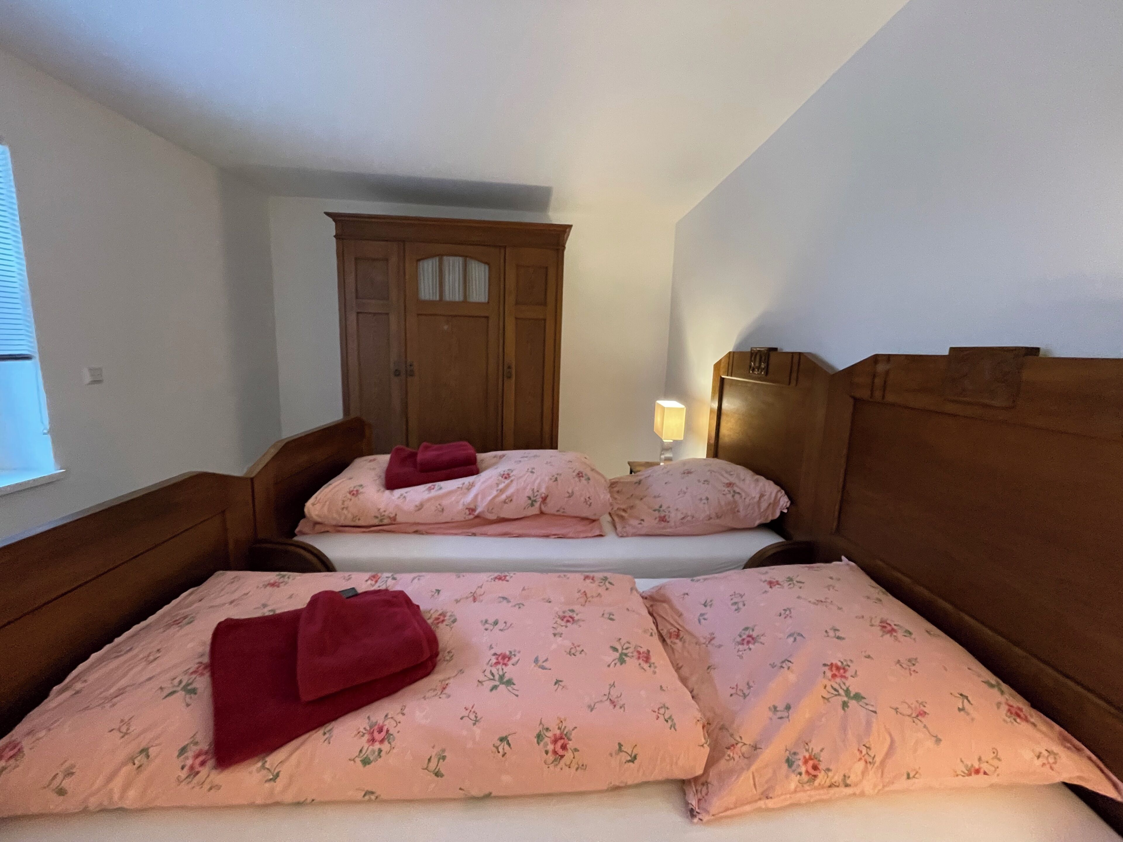 A bedroom with two beds, a wooden wardrobe, and a bedside lamp.