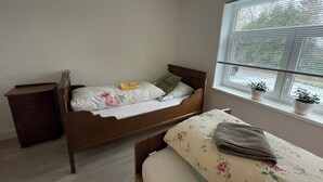Een enkel bed met bloemenbeddengoed, een nachtkastje, een raam met zonwering en een kleine potplant op de vensterbank.
