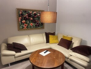 Ein Wohnzimmer mit einem beigefarbenen Ecksofa, einem runden Couchtisch aus Holz und einem Blumenbild an der Wand.