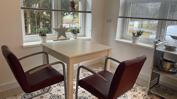 Een eethoek met een witte tafel en twee stoelen, een ster decoratie, en potplanten bij de ramen.