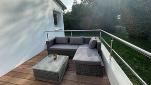 Een balkon met een rieten bank, een klein tafeltje en een metalen hekwerk.