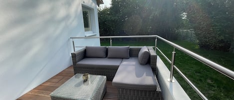 A balcony with a wicker sofa, a small table, and a metal railing.