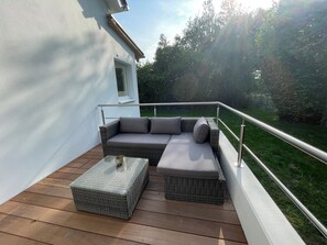 Ein Balkon mit einer Rattan-Couch, einem kleinen Tisch und einem Metallgeländer.