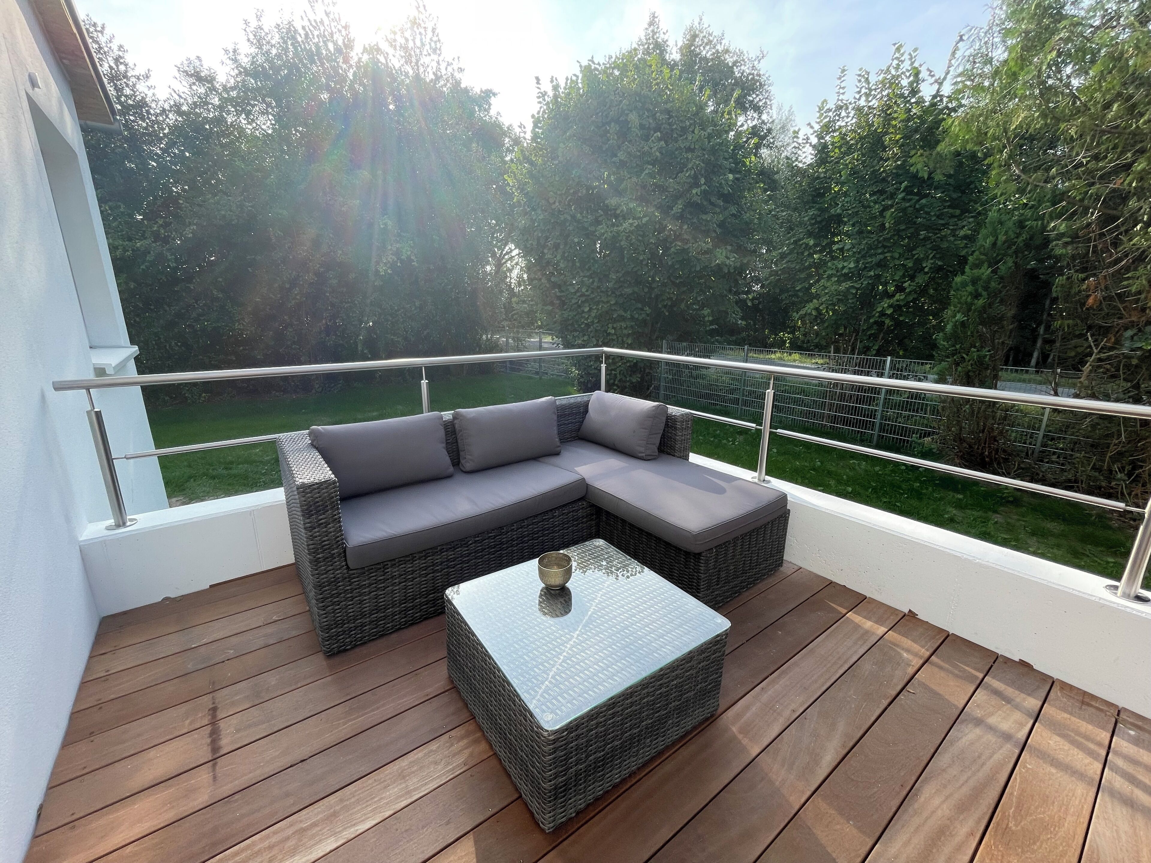 Ein Balkon mit einer Rattan-Couch und einem Glastisch, mit Blick auf eine grüne Landschaft.