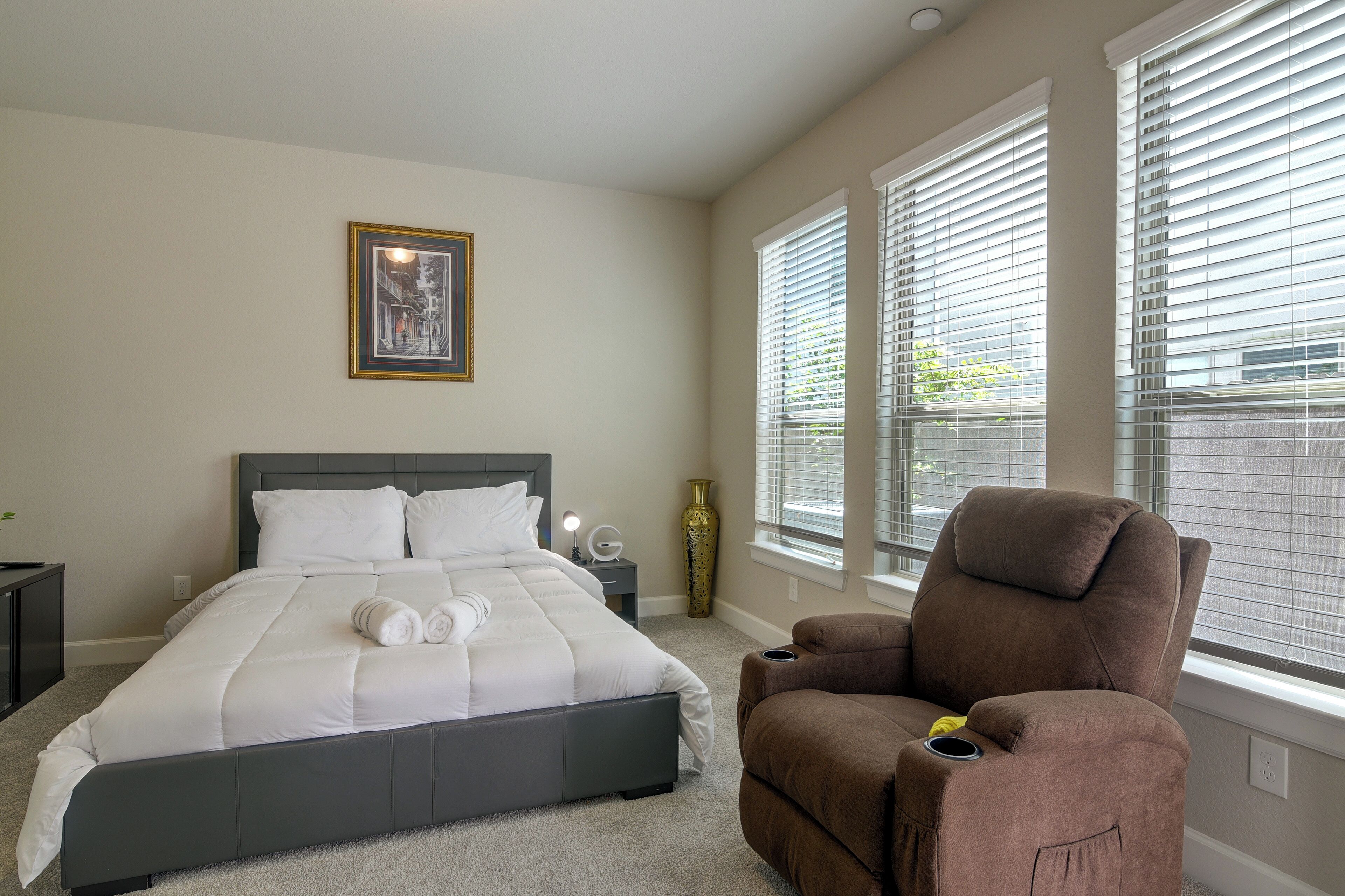 A bedroom with a bed, a chair, a nightstand, a vase, and a picture on the wall.