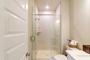 A modern bathroom with a glass-enclosed shower, a toilet, and a vanity with toiletries. - Modern Efficiency Studio Near NRG & Medical Center (Houston)