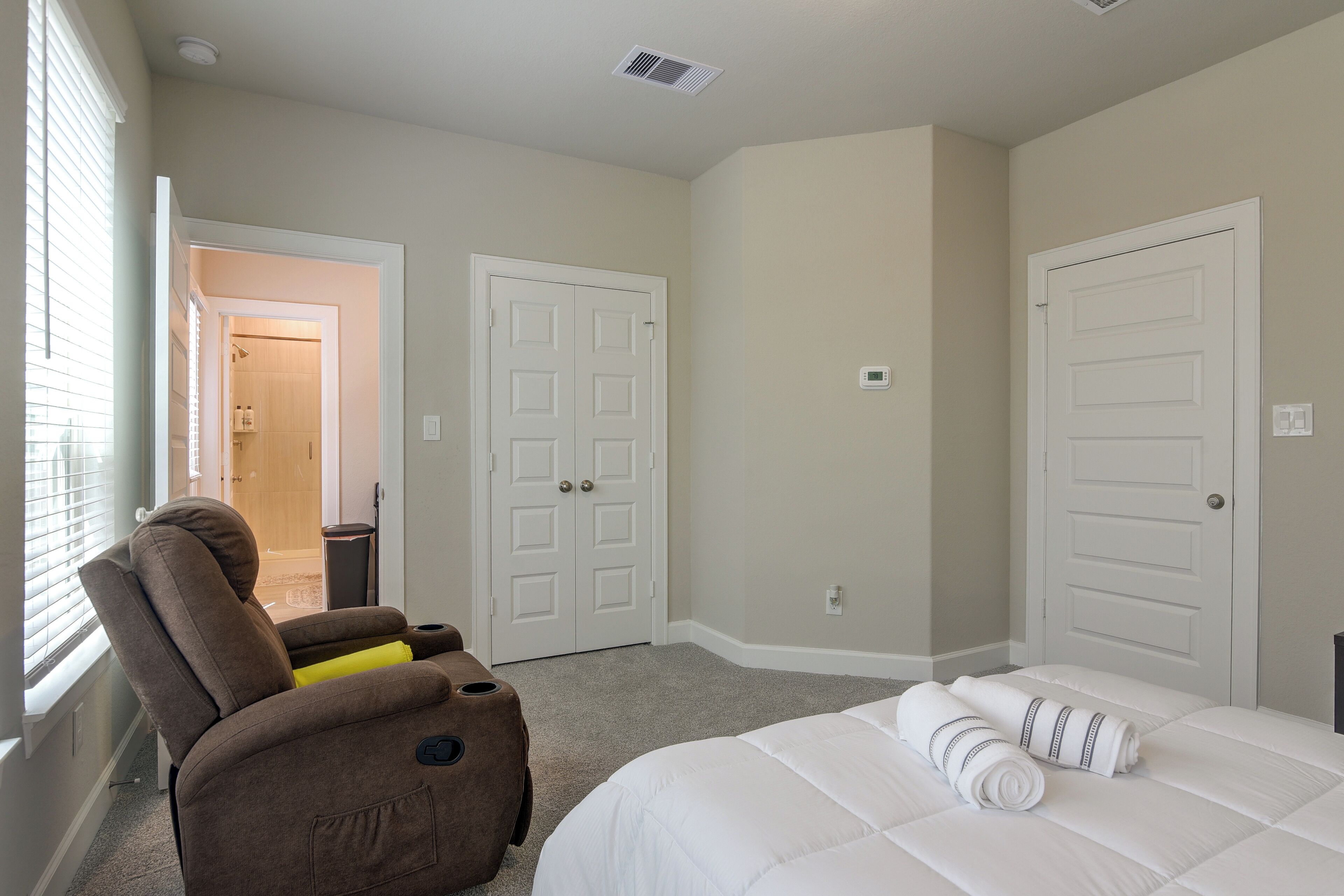 A bedroom with a bed, a chair, and two doors.
