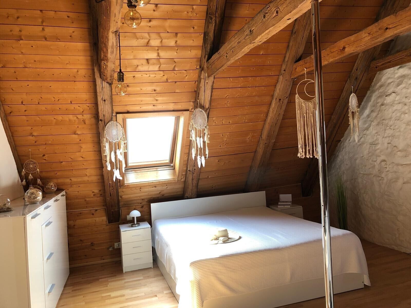 Ein Zimmer aus Holz mit einem Bett, einem Nachttisch, einer Kommode und einem Fenster mit Aussicht.