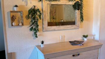A wooden vanity with a mirror, a small plant, and a welcome sign on the wall.