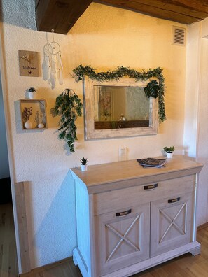 A wooden vanity with a mirror, a small plant, and a welcome sign on the wall.