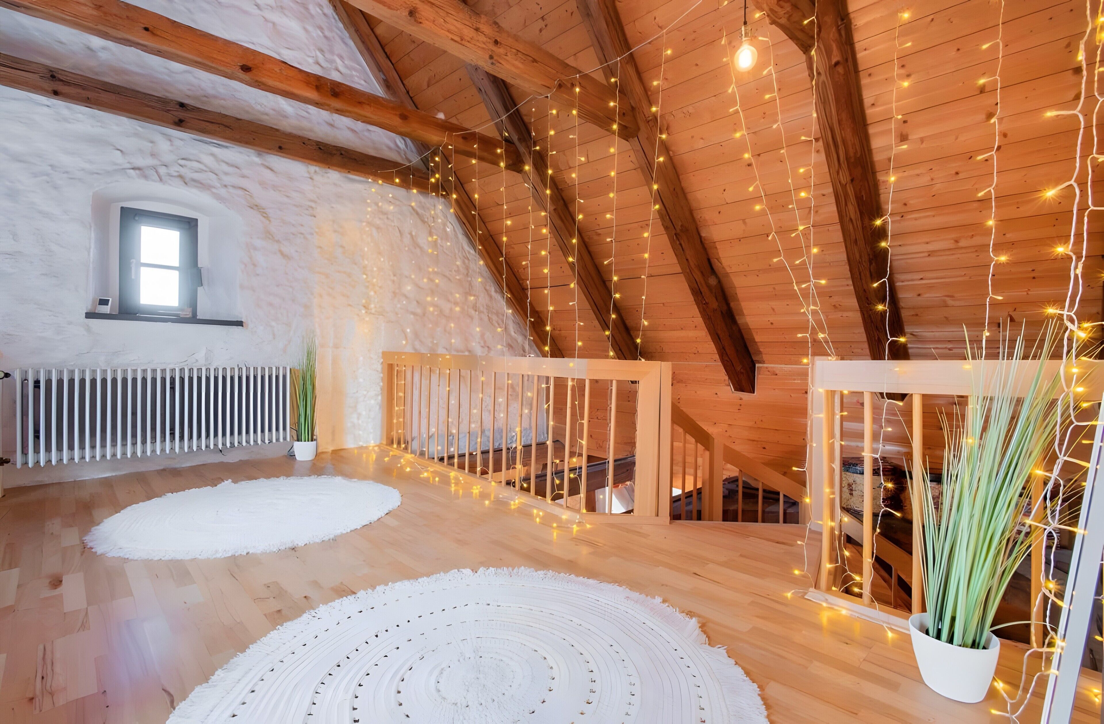 A cozy attic room with wooden beams, a white radiator, a small window, and a white circular rug.