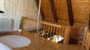 Ein Zimmer mit Holzbalken, hoher Decke, einem Bett mit weißer gesteppter Bettdecke, zwei Häkelteppichen und Lichterketten.