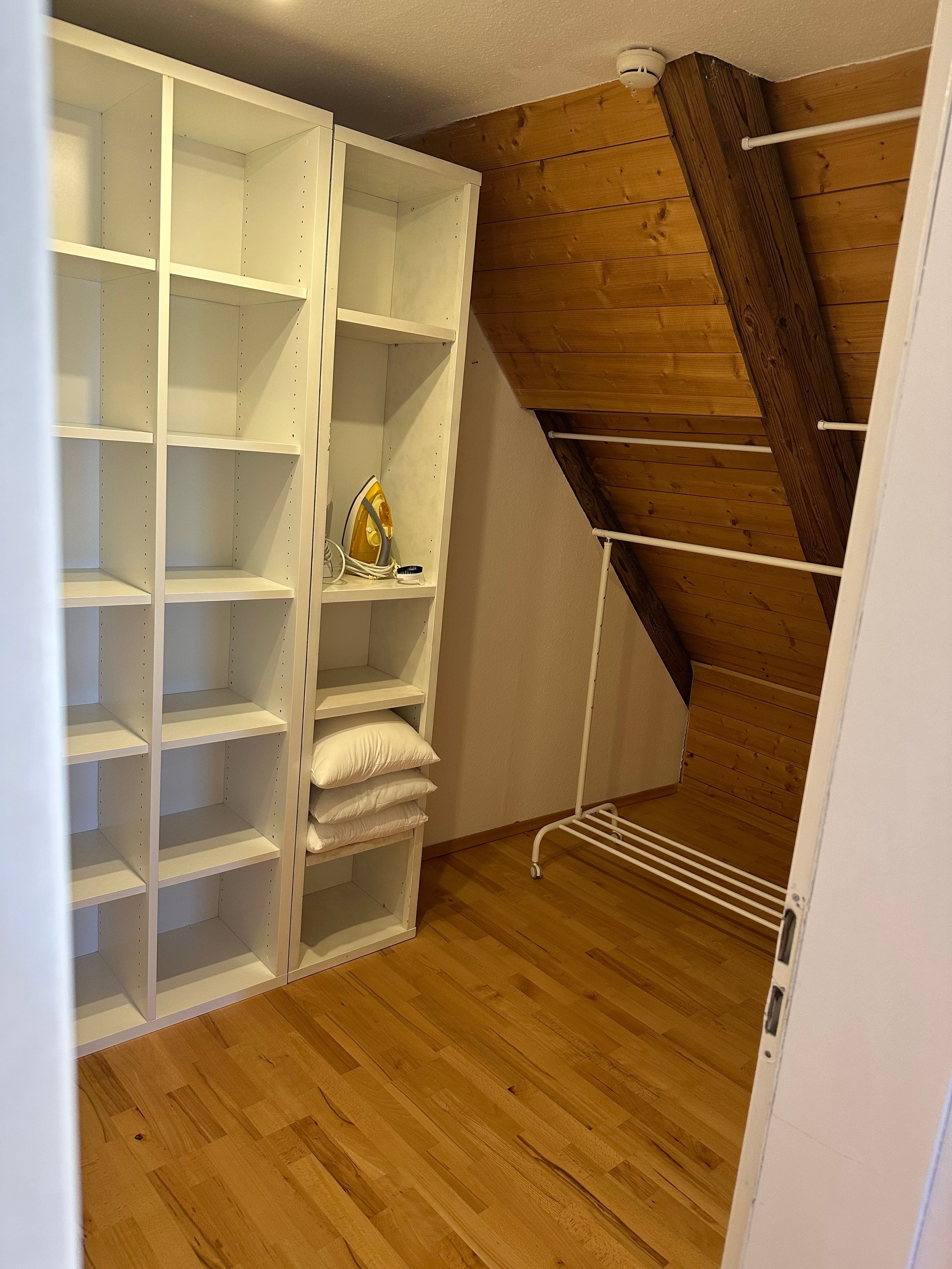 Ein begehbarer Kleiderschrank mit mehreren Regalen und einer Kleiderstange, Holzboden und einer geneigten Decke.