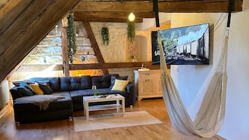 Ein Loft-Wohnzimmer mit Holzbalkendecke, einem schwarzen Ecksofa, einem weißen Couchtisch und einer Hängematte.