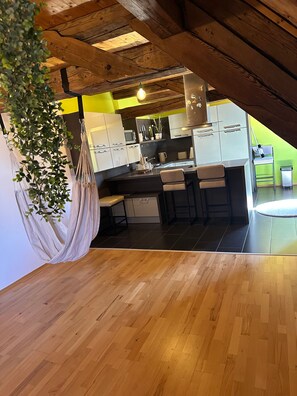A modern kitchen with wooden beams, a hanging macrame chair, and a green wall.