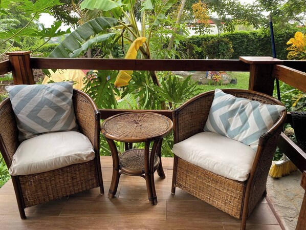 A wicker chair and sofa set with cushions, a small round table, and a view of lush greenery.