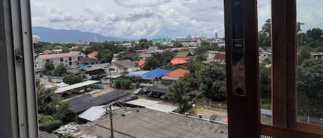 Vista desde una ventana sobre una zona residencial con casas, un pequeño mercado y una cadena montañosa distante.