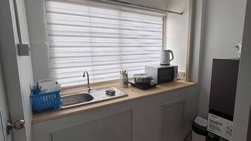 Una kitchenette compacta con un lavamanos, una cafetera y un pequeño cubo de basura.