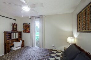 Ein Schlafzimmer mit einem Bett, einem Deckenventilator, einem Gemälde, einer Uhr und einem Fenster mit Vorhängen.