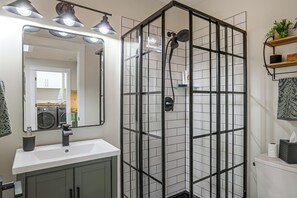 Et moderne badeværelse med en glasafskærmet brusekabine, en vask med et spejl over, og et toilet med et håndklæde hængende på væggen.
