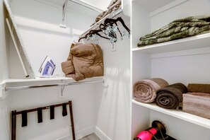 Ein Waschbereich mit aufgehängter Kleidung, einem Bügelbrett und einem Regal mit gerollten Handtüchern.
