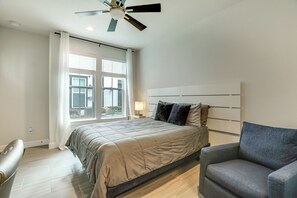 Een slaapkamer met een bed, een stoel, een plafondventilator en een raam met jaloezieën.