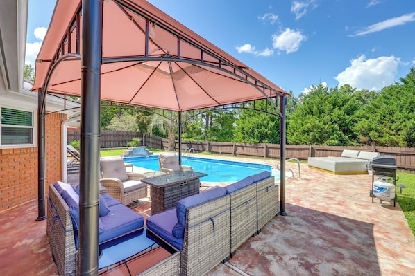 Ein Garten mit überdachter Sitzgelegenheit, einem Schwimmbecken und einem Grill.