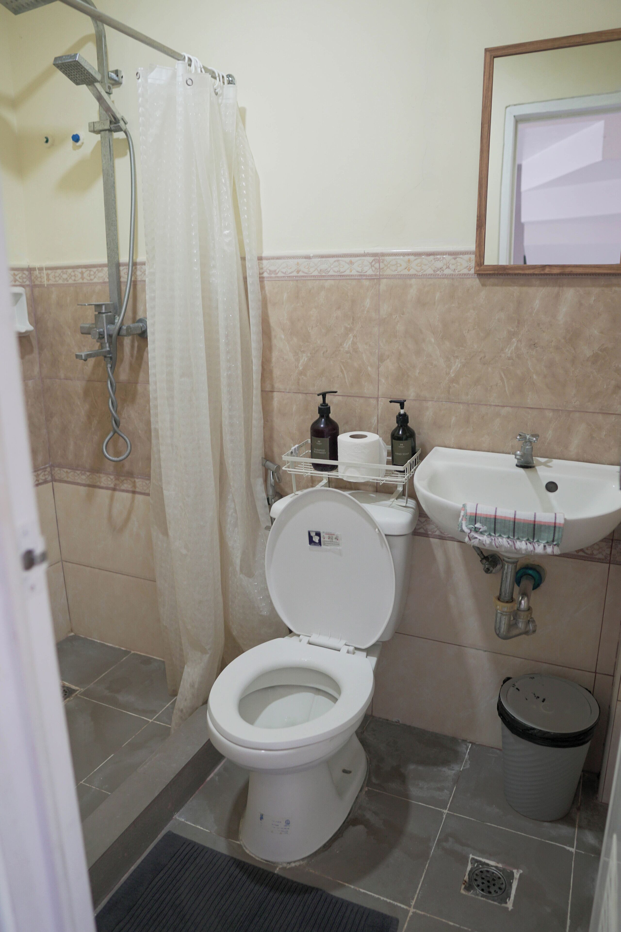Baño con inodoro, ducha, lavamanos y cubo de basura.