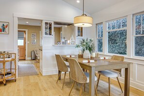 A dining area with a wooden table, wicker chairs, and a hanging light fixture. - Stroll to Redondo Beach: Modern, Coastal Gem (Redondo Beach)