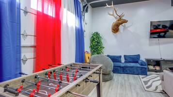 Une pièce comprenant une table de baby-foot, une tête de cerf accrochée au mur, un canapé et un téléviseur.