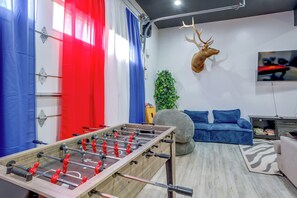 Una habitación con una mesa de fútbol de mesa, una cabeza de venado decorativa, un sofá y un televisor.